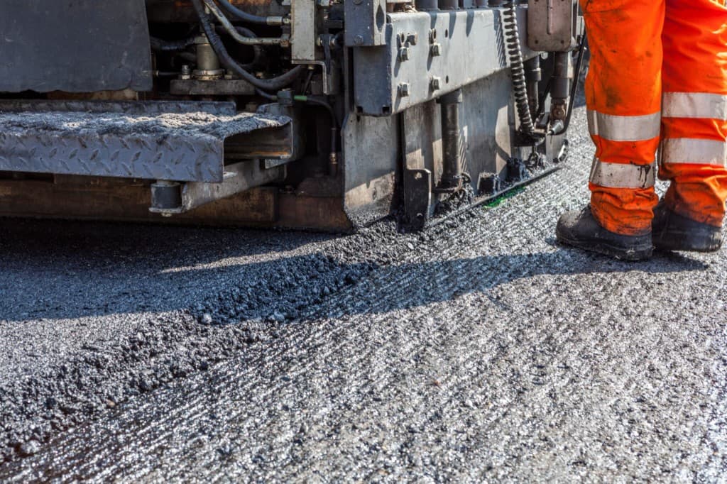 Close-up of asphalt paver laying fresh hot-mix next to milled surface with A-1 Asphalt Paving crew in hi-vis orange in Piscataway, NJ